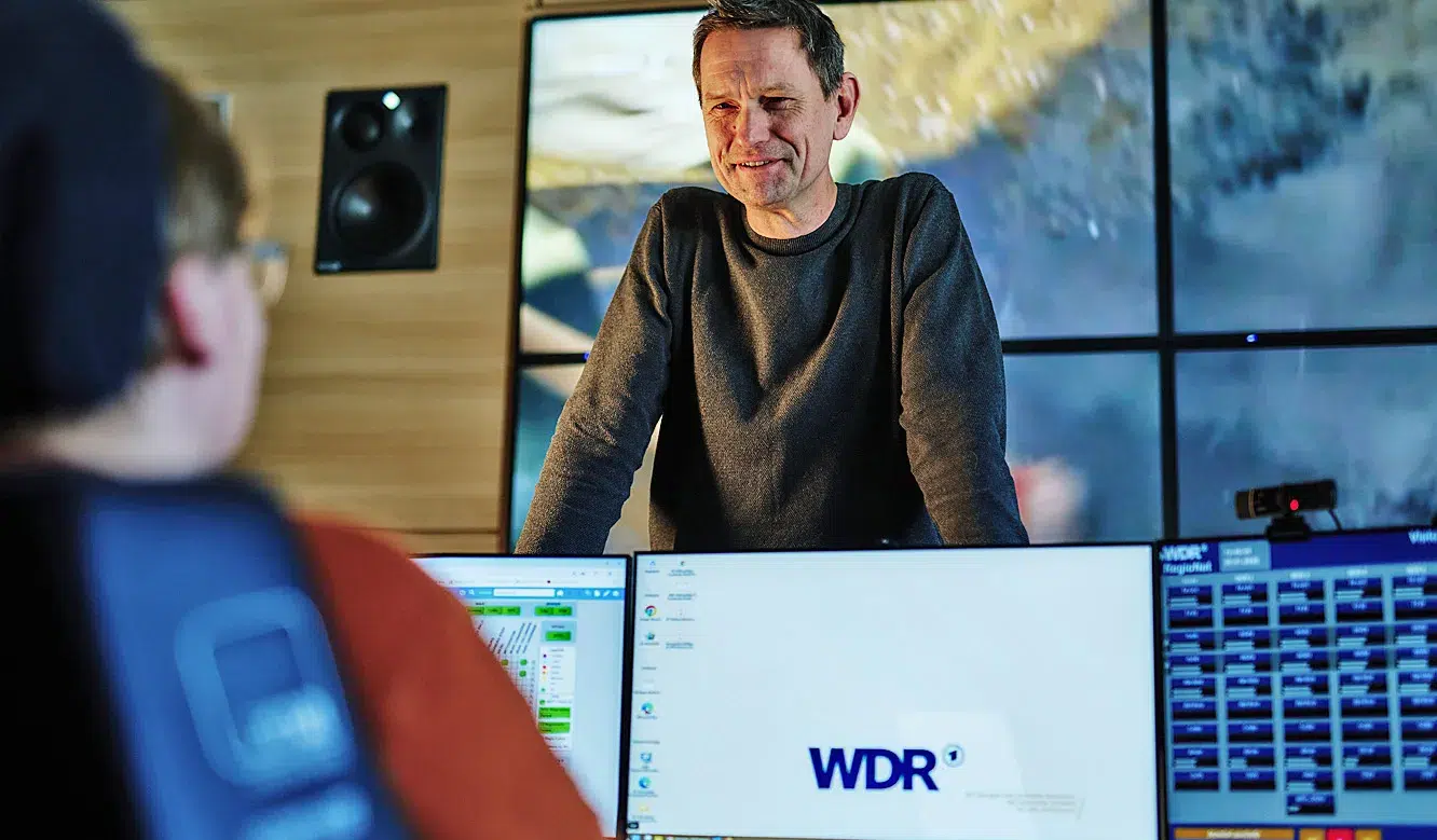 JST Referenz NOC Betriebszentrum WDR: Oliver Konschak spricht mit Operator im Kontrollraum mit vielen Monitoren